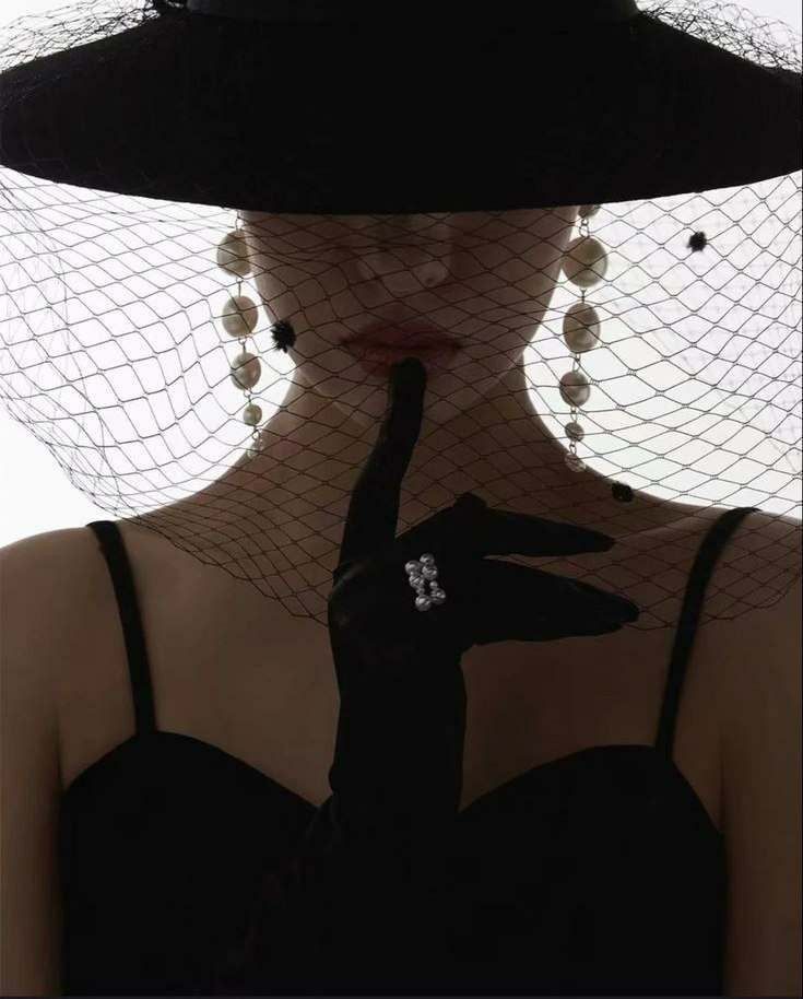 A veiled hat and a gloved finger to the lips